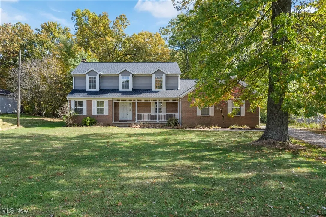 View of front facade featuring a porch, brick siding, a front lawn, and a chimney