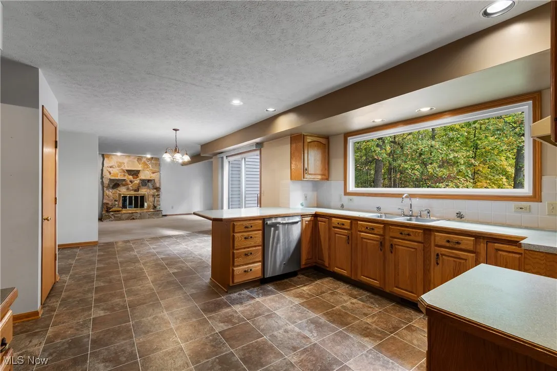 Kitchen with light countertops, a stone fireplace, a peninsula, a textured ceiling, and stainless steel dishwasher