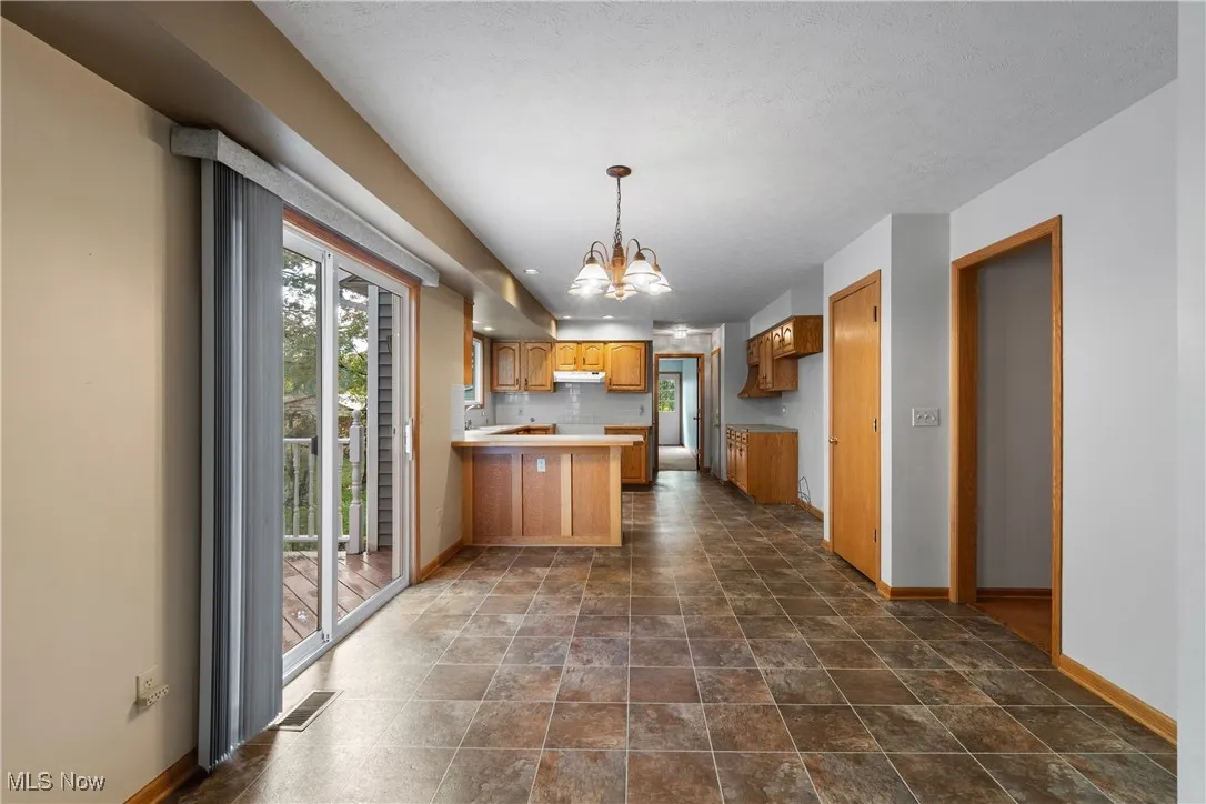 Kitchen with healthy amount of natural light, a peninsula, a chandelier, and decorative backsplash