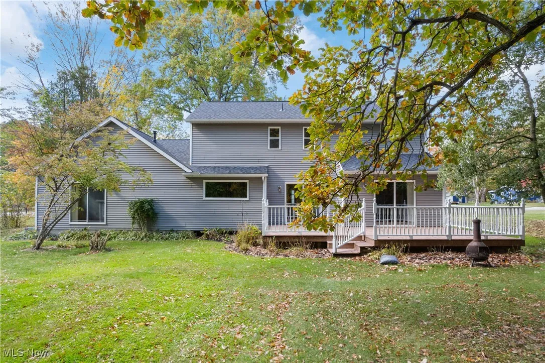Back of property with a lawn, a wooden deck, and a shingled roof