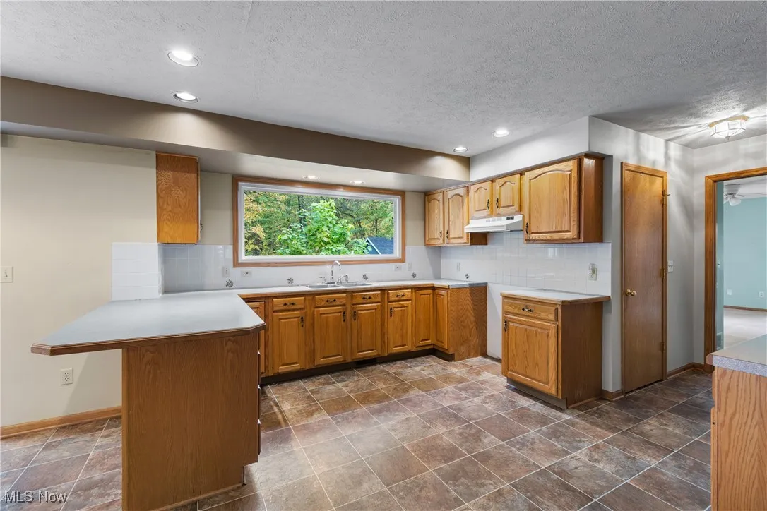 Kitchen featuring brown cabinets, a peninsula, light countertops, a textured ceiling, and backsplash