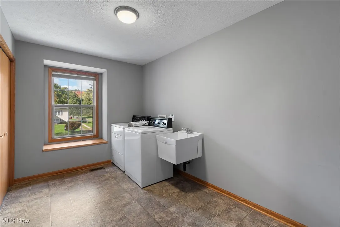 Washroom with a textured ceiling, washing machine and clothes dryer, and stone finish flooring