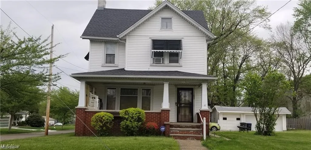 View of front of property with a front yard, roof with shingles, brick siding, a chimney, and a porch