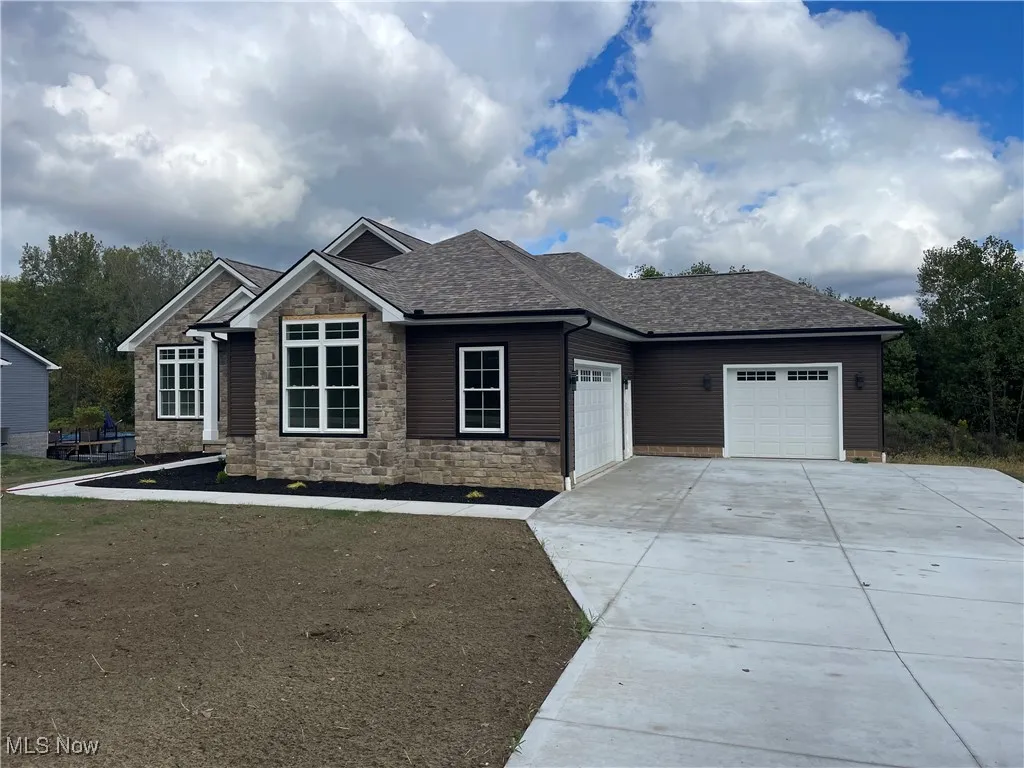 Craftsman-style house featuring roof with shingles, driveway, stone siding, and an attached garage