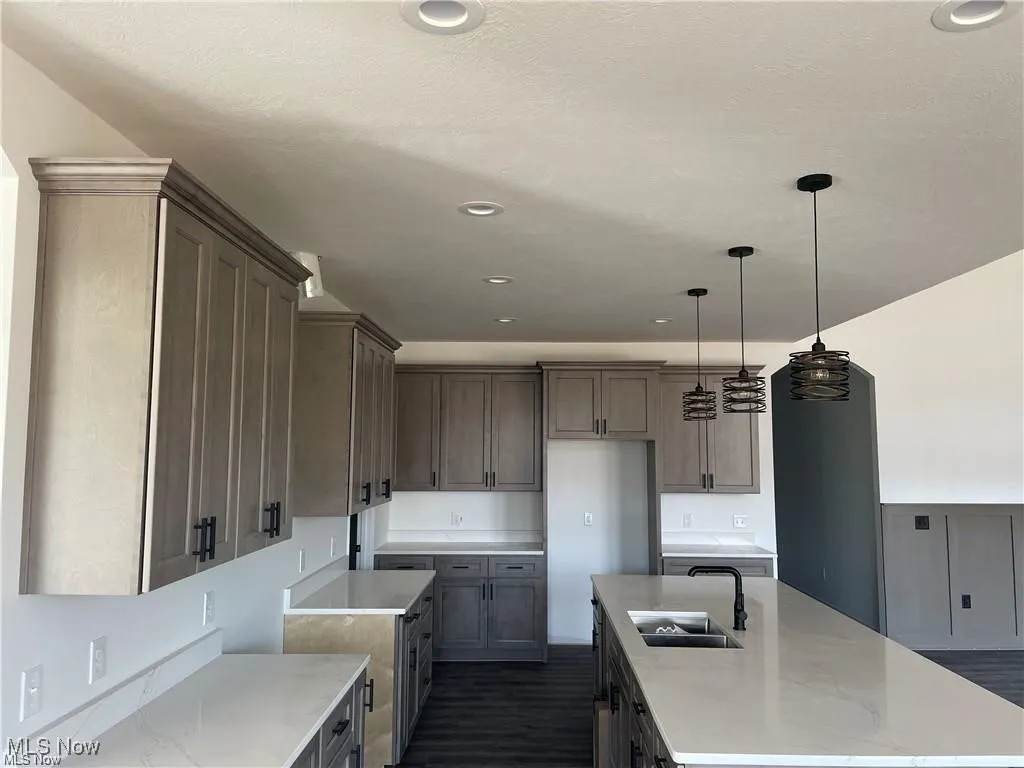 Kitchen featuring an island with sink, light stone counters, pendant lighting, and recessed lighting