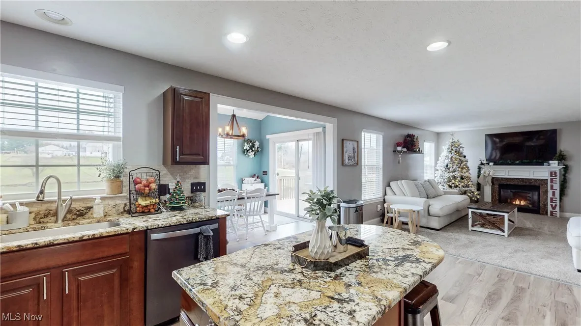 Kitchen with stainless steel dishwasher, light stone counters, open floor plan, a glass covered fireplace, and recessed lighting