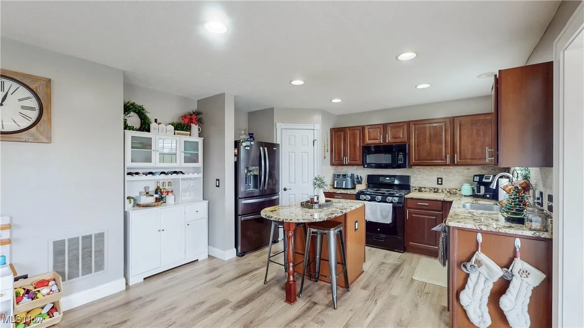 Kitchen with a kitchen breakfast bar, black appliances, light stone counters, light wood-type flooring, and recessed lighting