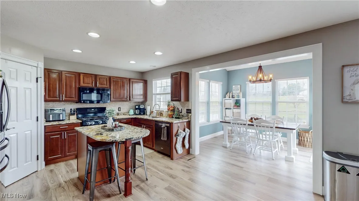 Kitchen with a kitchen breakfast bar, tasteful backsplash, light stone countertops, black appliances, and light wood-style flooring