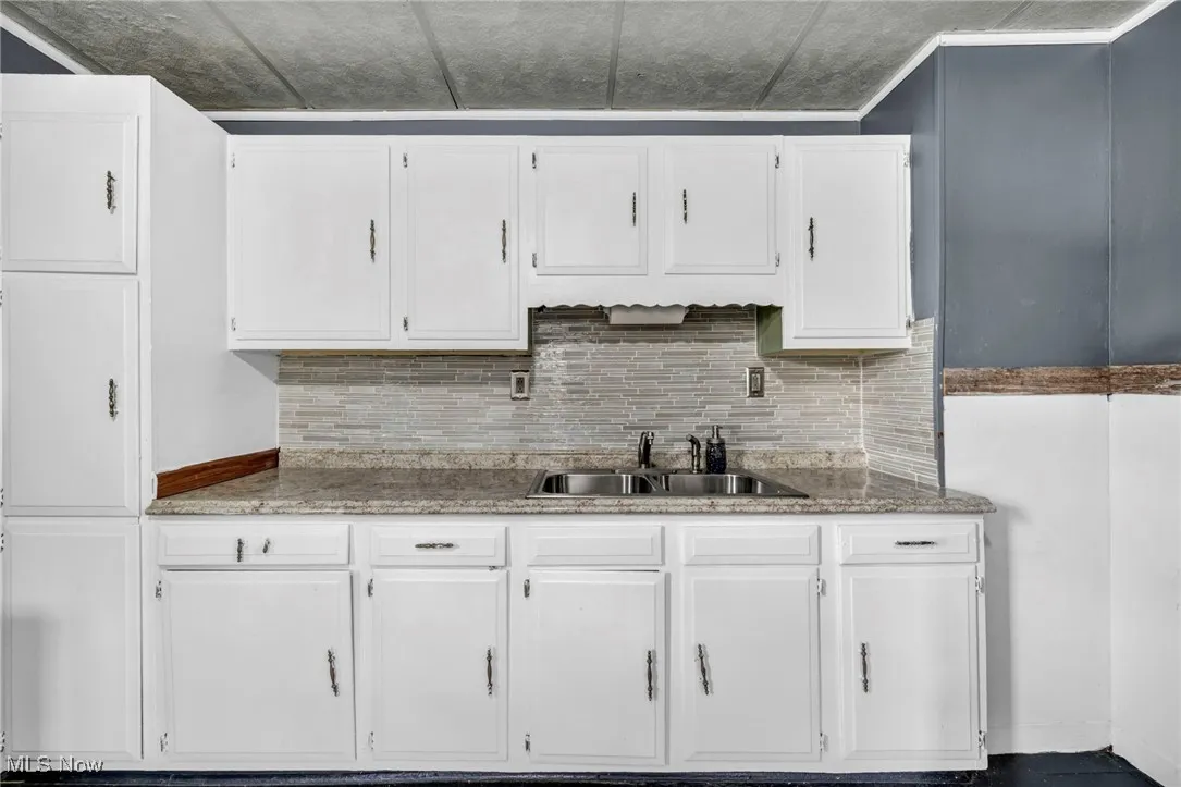 Kitchen featuring white cabinets, decorative backsplash, and dark stone countertops