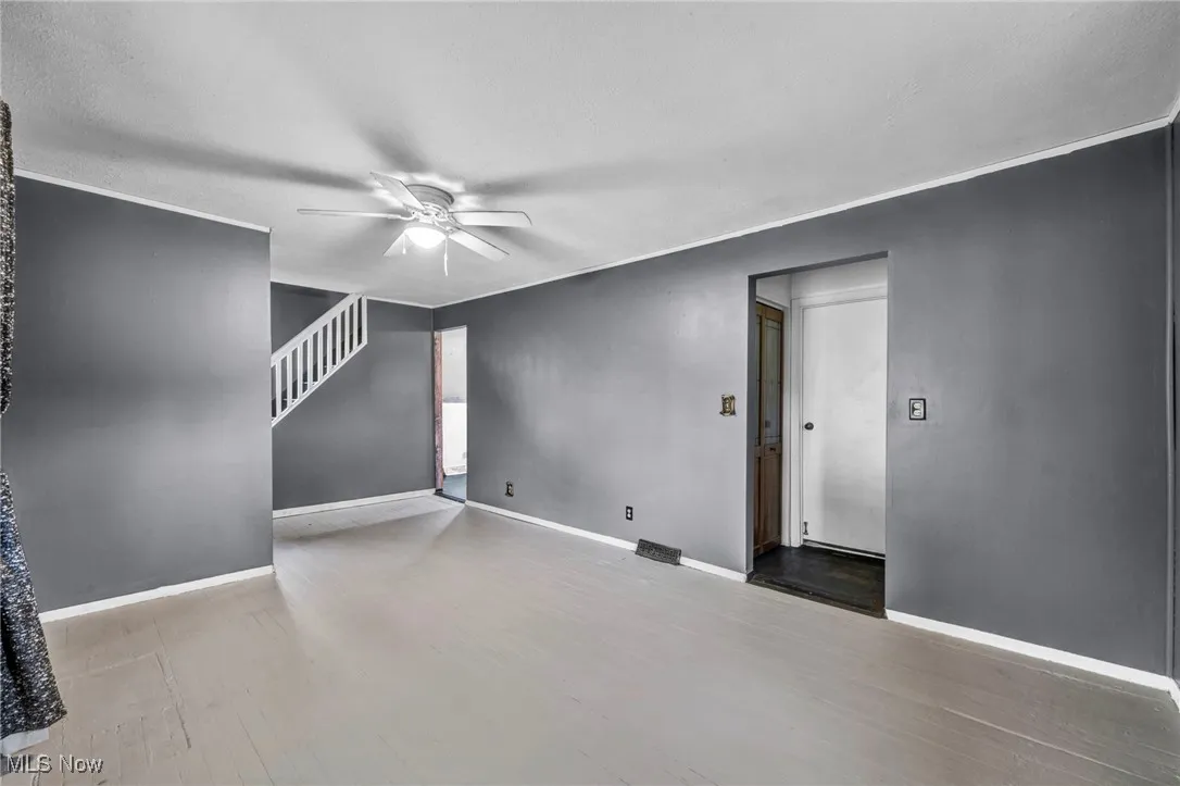 Unfurnished living room with a ceiling fan, light wood-style floors, crown molding, a textured ceiling, and stairs