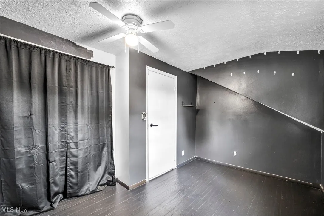 Unfurnished bedroom with a textured ceiling, dark wood-style flooring, and a ceiling fan