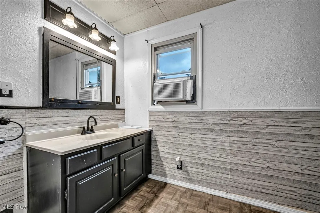 Bathroom with a textured wall, a wainscoted wall, vanity, and cooling unit