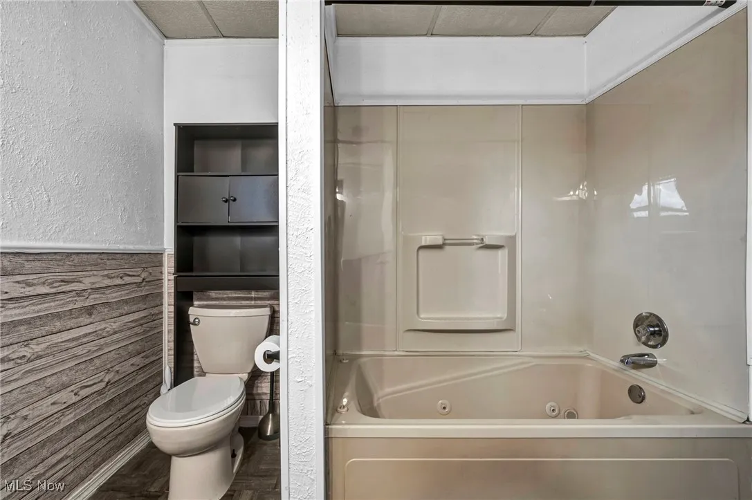 Full bath with a combined bath / shower with jetted tub, a textured wall, a wainscoted wall, and wooden walls