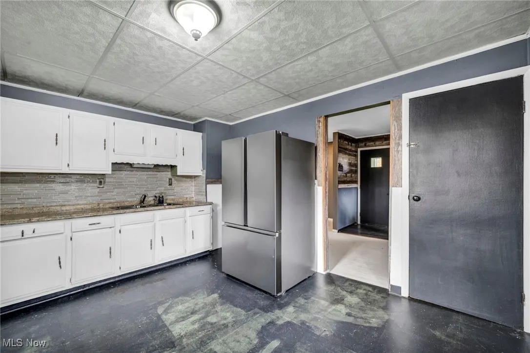 Kitchen with freestanding refrigerator, white cabinets, decorative backsplash, light stone countertops, and a drop ceiling