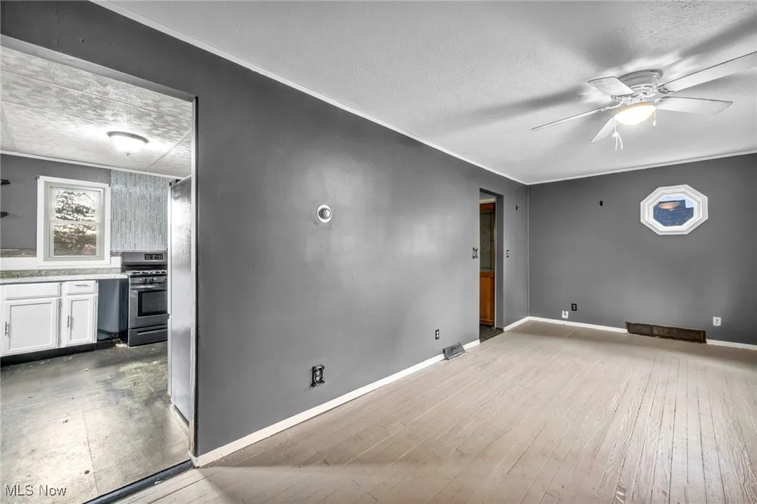 Unfurnished room featuring a textured ceiling, ornamental molding, light wood-style flooring, and ceiling fan