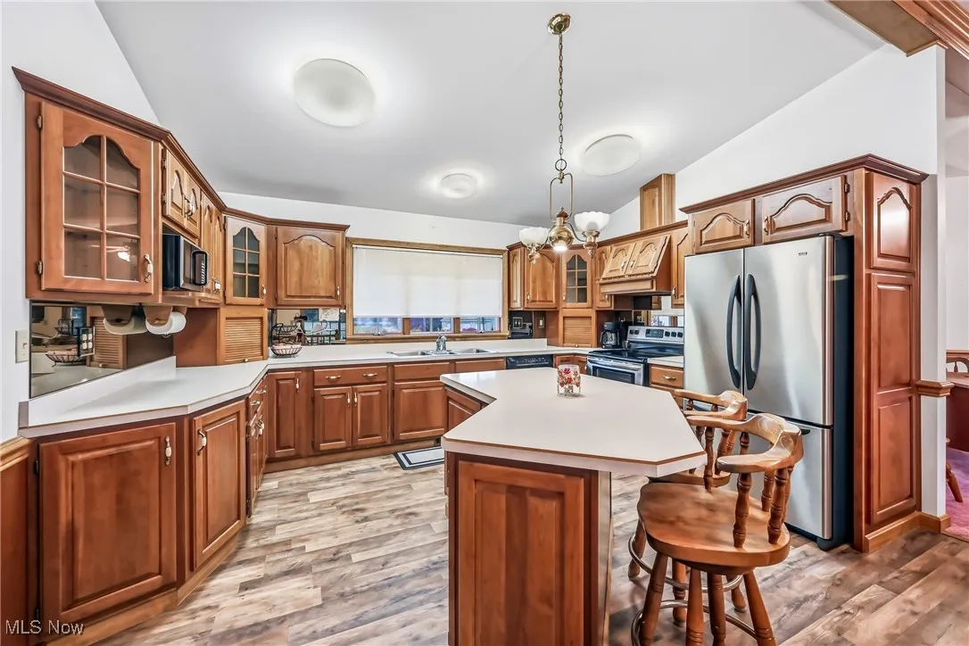 Kitchen featuring glass insert cabinets, light countertops, appliances with stainless steel finishes, brown cabinetry, and a kitchen breakfast bar