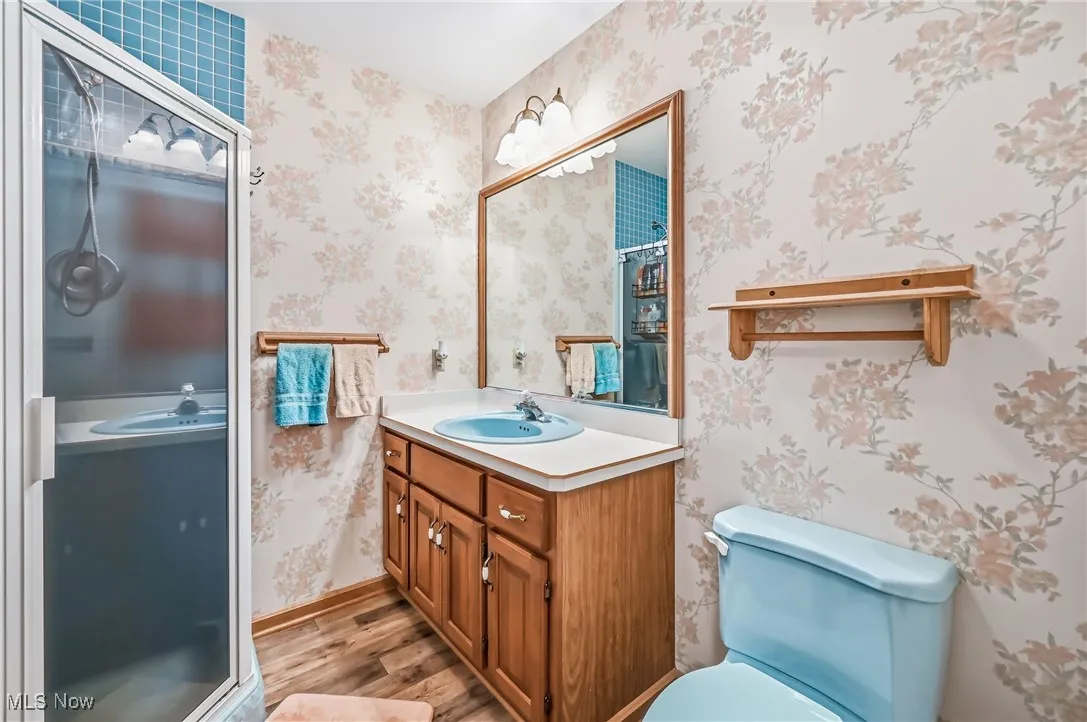 Bathroom with wallpapered walls, vanity, light wood finished floors, and a shower stall