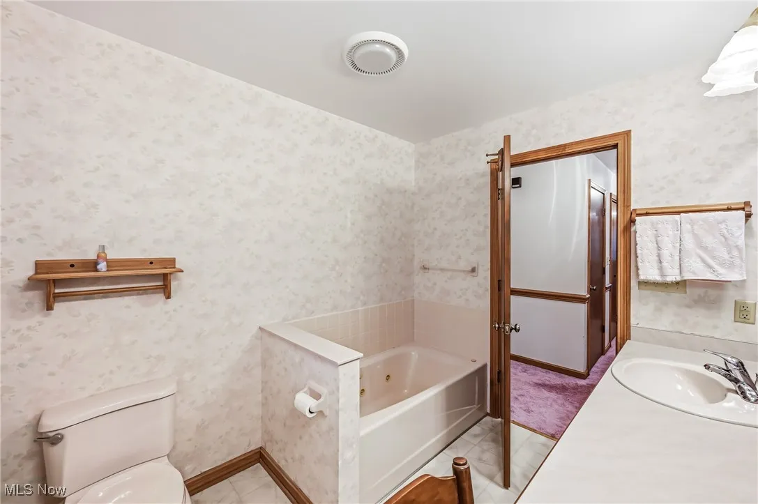 Bathroom featuring a jetted tub, vanity, wallpapered walls, and light tile patterned flooring