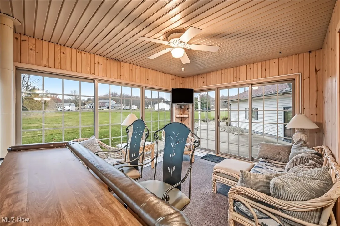 Carpeted living area featuring a ceiling fan, a residential view, wooden walls, and wood ceiling