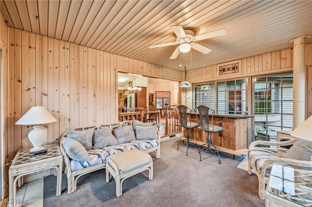 Living room with wooden walls, a ceiling fan, and wood ceiling
