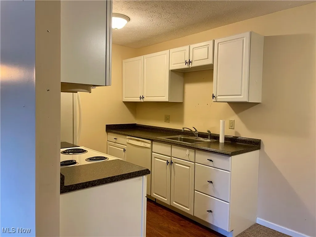 Kitchen with white cabinetry, dark countertops, dark wood-style flooring, a textured ceiling, and white appliances