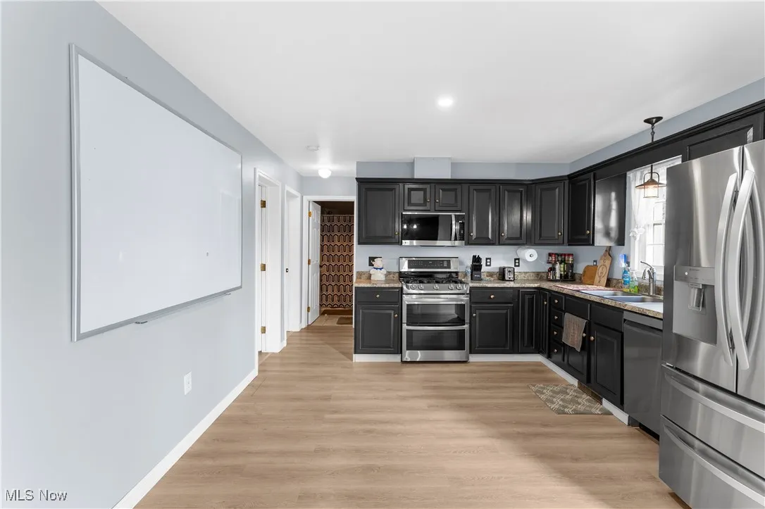 Kitchen with appliances with stainless steel finishes, light wood-type flooring, dark cabinets, decorative light fixtures, and recessed lighting