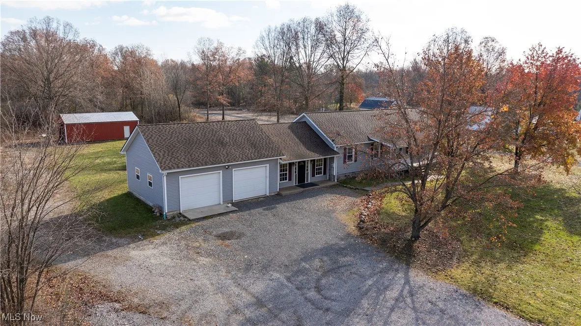 View of front of property featuring gravel driveway, a shingled roof, a front yard, and a garage