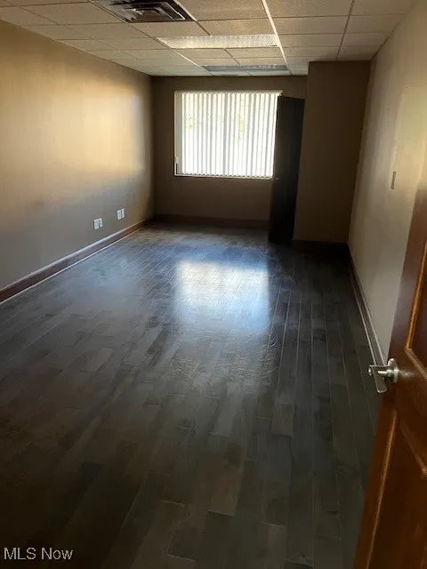 Empty room featuring a paneled ceiling and dark wood-style floors