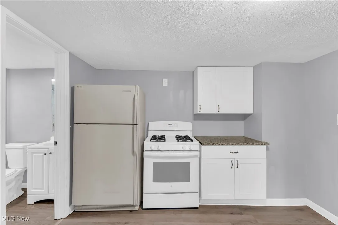 Kitchen featuring white appliances, a textured ceiling, white cabinets, light wood-type flooring, and dark stone countertops