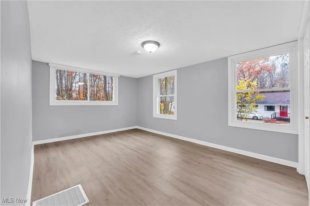 Empty room with a textured ceiling, light wood finished floors, and plenty of natural light