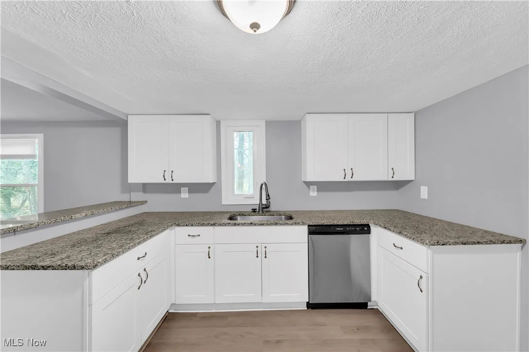 Kitchen featuring light stone countertops, stainless steel dishwasher, a peninsula, light wood-style flooring, and white cabinets