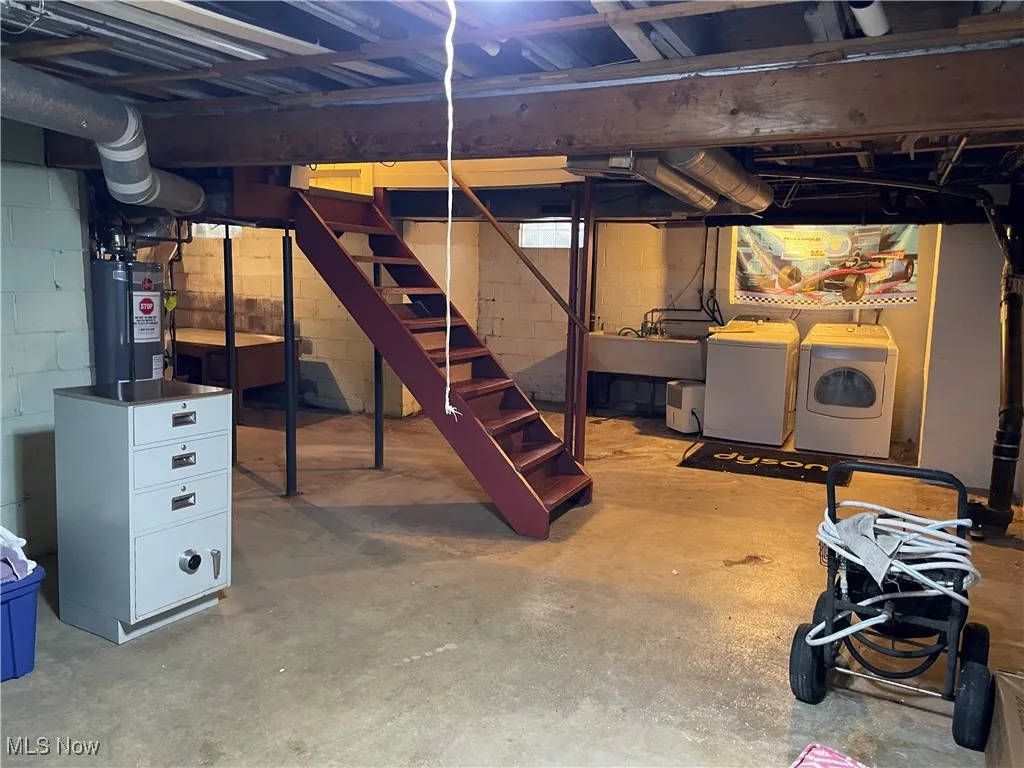 Unfinished basement featuring washer and clothes dryer, stairs, and water heater