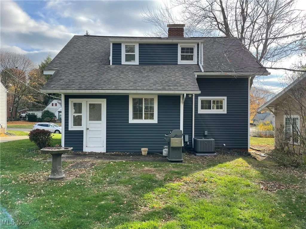 Rear view of house featuring a yard, roof with shingles, and a chimney
