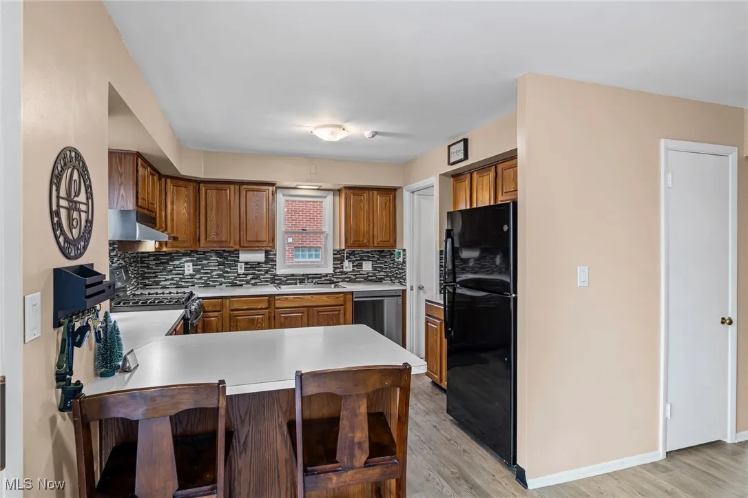 Kitchen with a peninsula, light countertops, freestanding refrigerator, decorative backsplash, and range with gas stovetop