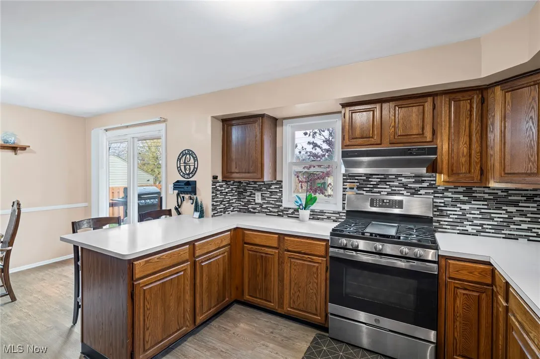 Kitchen featuring gas range, light countertops, tasteful backsplash, light wood-type flooring, and under cabinet range hood