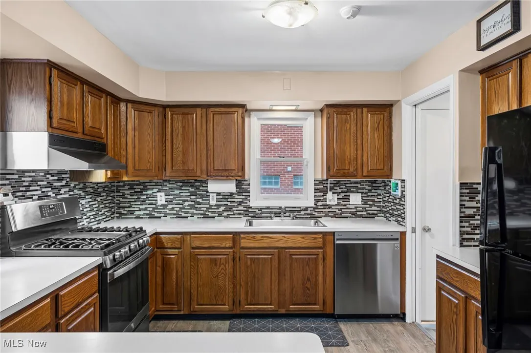 Kitchen with stainless steel appliances, light countertops, under cabinet range hood, and brown cabinets