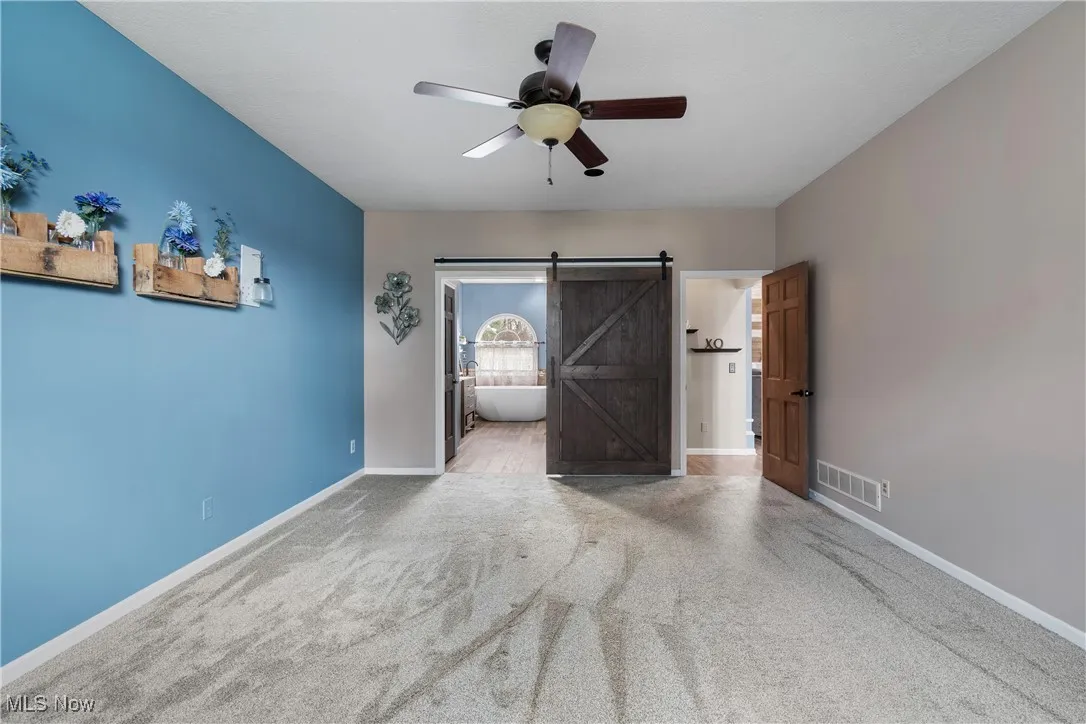 Unfurnished bedroom featuring carpet floors, a barn door, and a ceiling fan