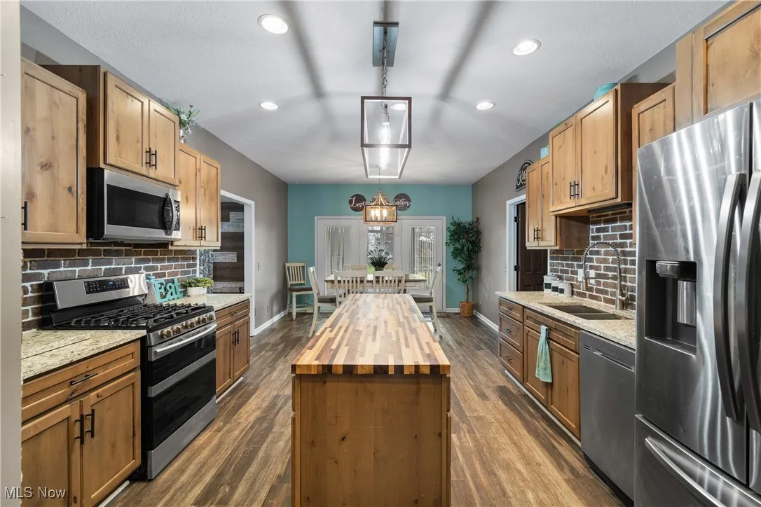 Kitchen featuring decorative backsplash, appliances with stainless steel finishes, butcher block counters, hanging light fixtures, and recessed lighting