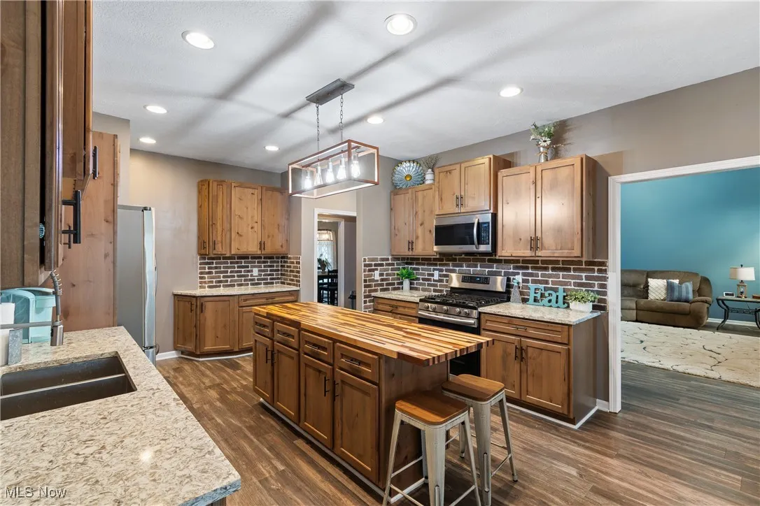 Kitchen with wooden counters, brown cabinets, hanging light fixtures, appliances with stainless steel finishes, and dark wood-type flooring