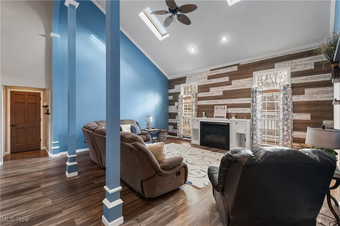 Living area featuring a skylight, high vaulted ceiling, ornamental molding, dark wood finished floors, and wooden walls