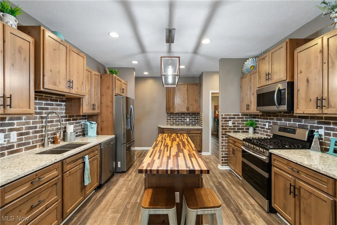 Kitchen featuring light stone countertops, stainless steel appliances, pendant lighting, dark wood-type flooring, and tasteful backsplash