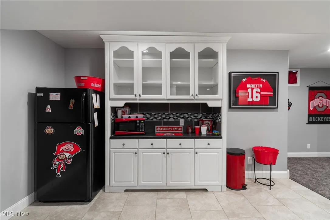 Kitchen with dark countertops, freestanding refrigerator, white cabinets, and backsplash