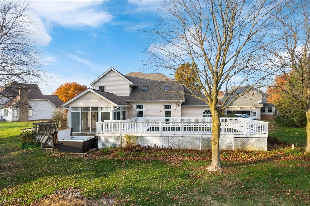 Rear view of house featuring a sunroom, a lawn, a wooden deck, and roof with shingles