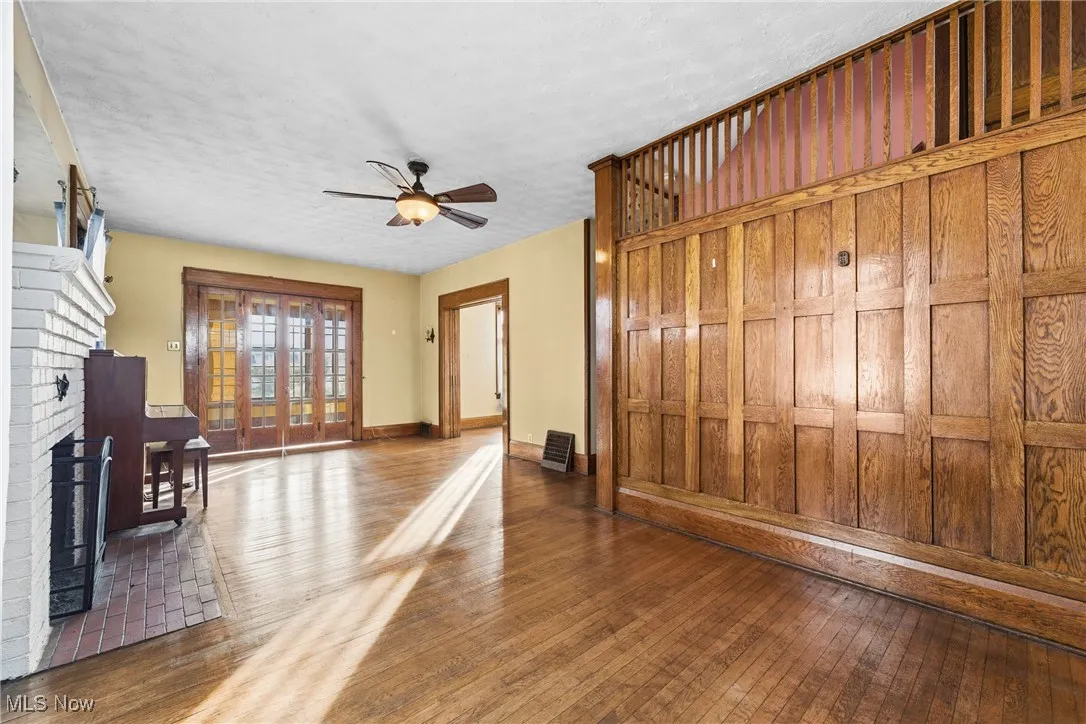 Unfurnished living room featuring hardwood / wood-style flooring, a ceiling fan, a brick fireplace, and a textured ceiling