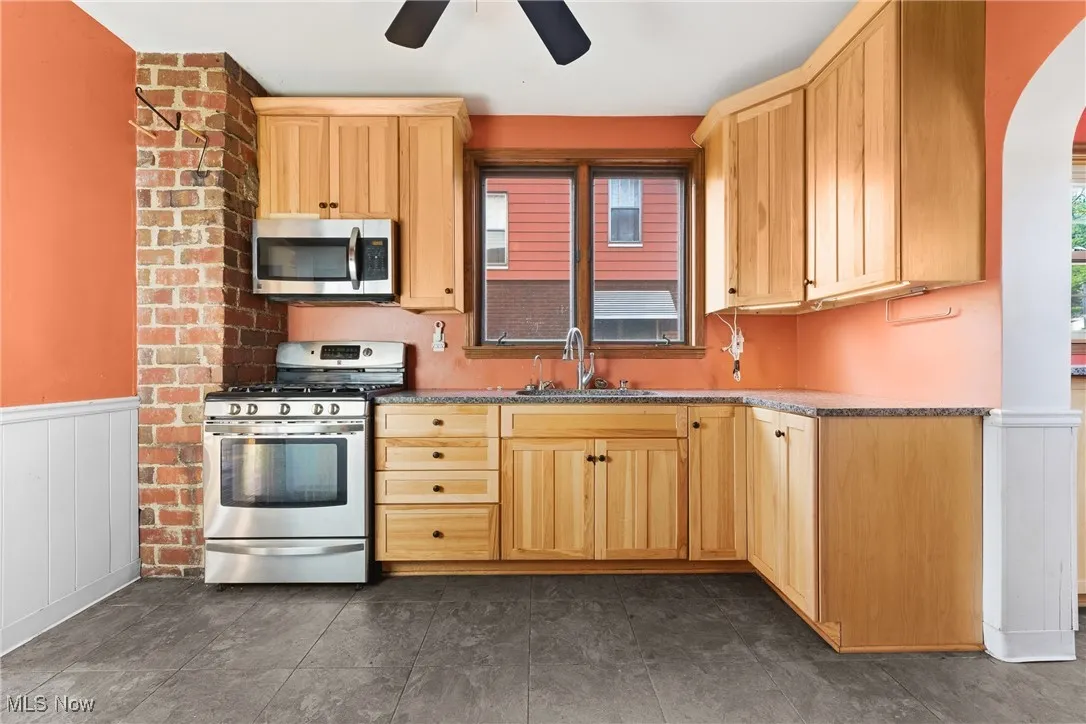 Kitchen with wainscoting, stainless steel appliances, light brown cabinetry, dark stone counters, and a ceiling fan