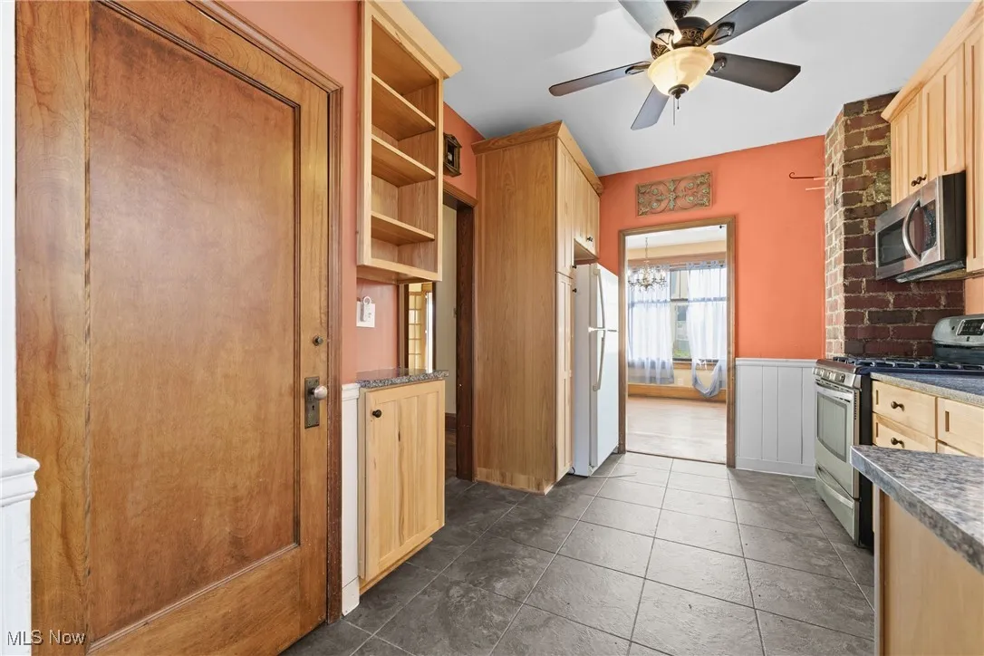 Kitchen featuring stainless steel appliances, open shelves, light brown cabinetry, a chandelier, and wainscoting
