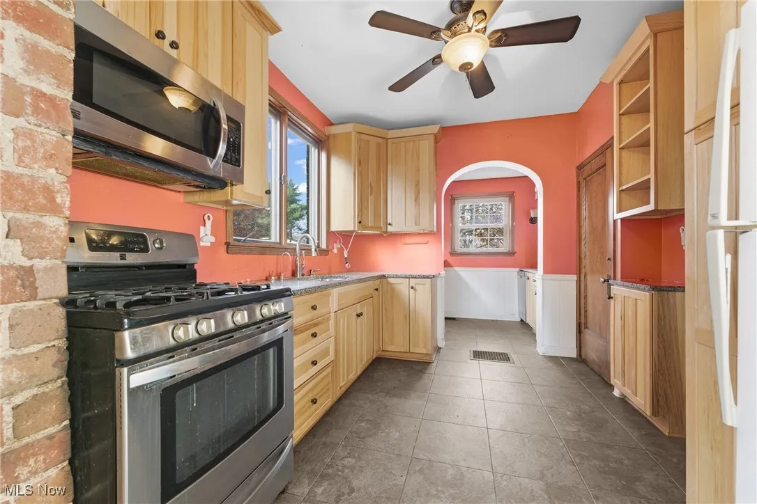 Kitchen with light brown cabinets, stainless steel appliances, arched walkways, healthy amount of natural light, and wainscoting