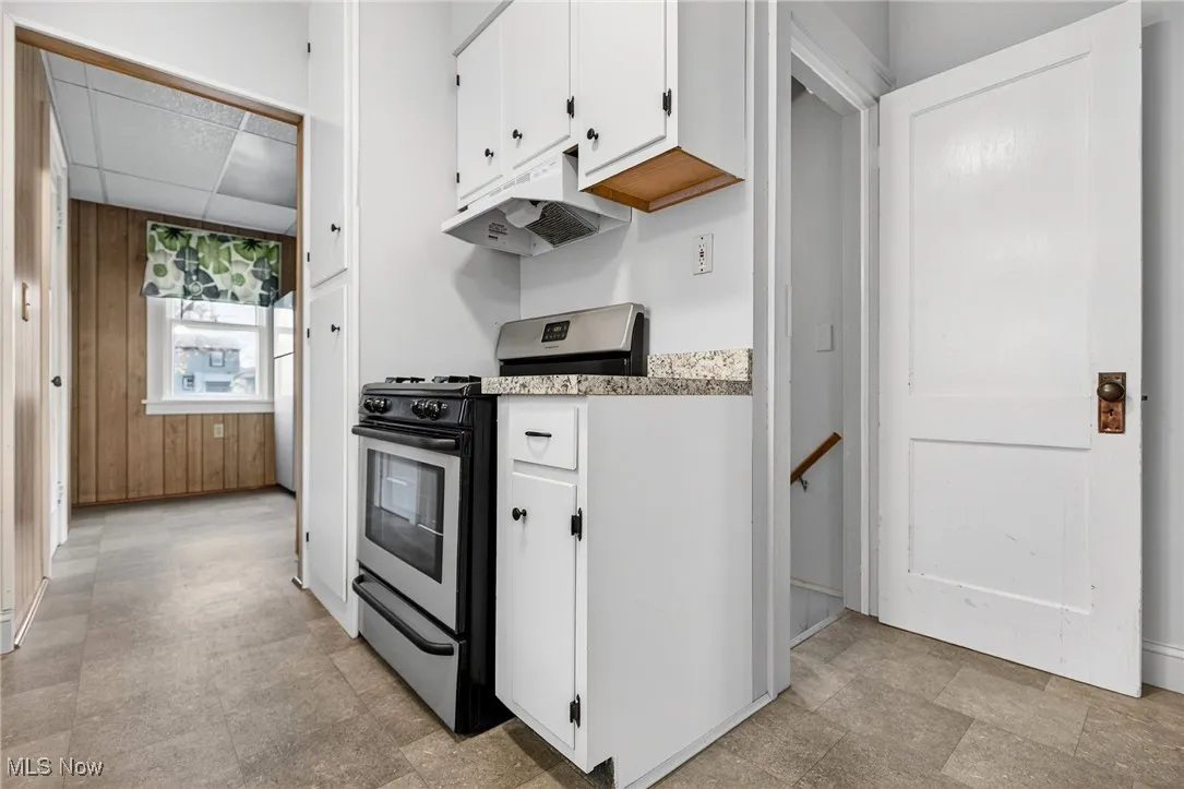 Kitchen with stainless steel range with gas stovetop, white cabinets, under cabinet range hood, a paneled ceiling, and light stone counters