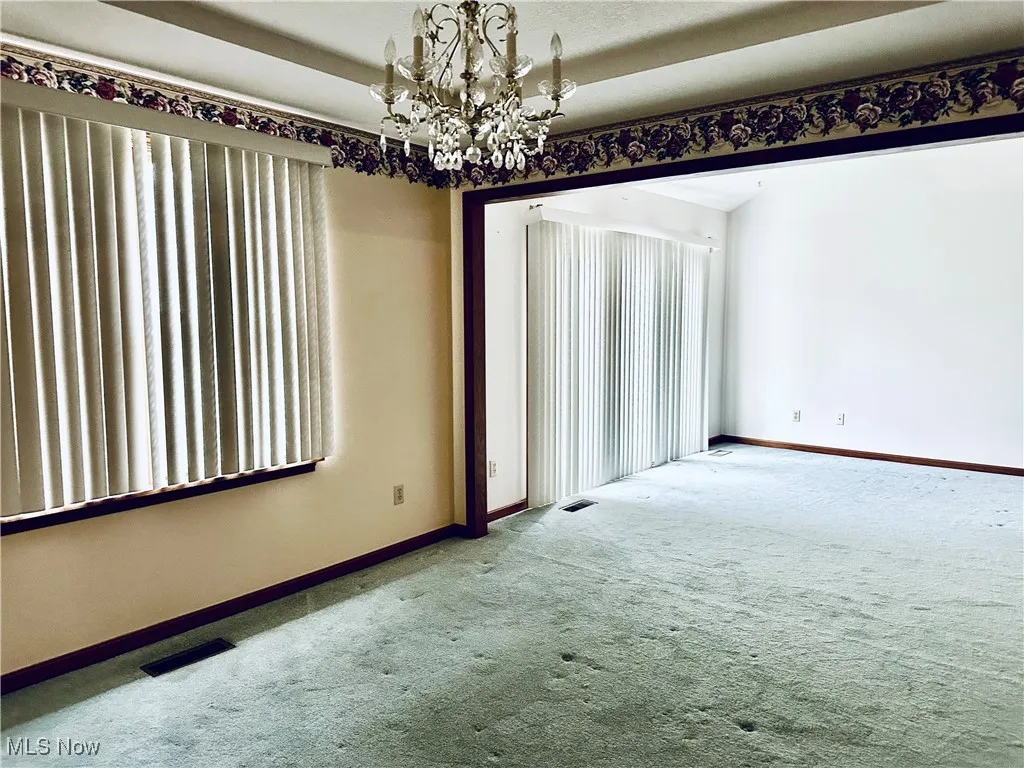 Carpeted spare room with a chandelier and baseboards