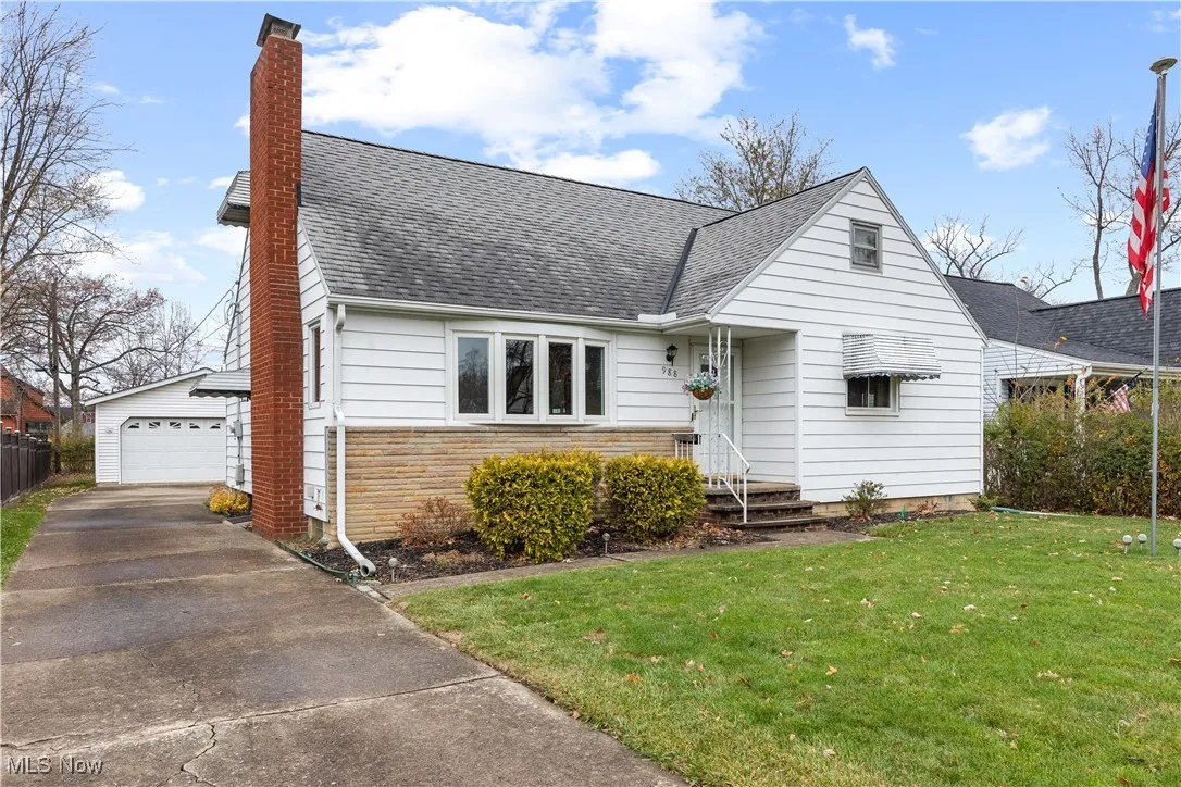 View of front of property featuring a shingled roof, a front yard, a chimney, stone siding, and a garage